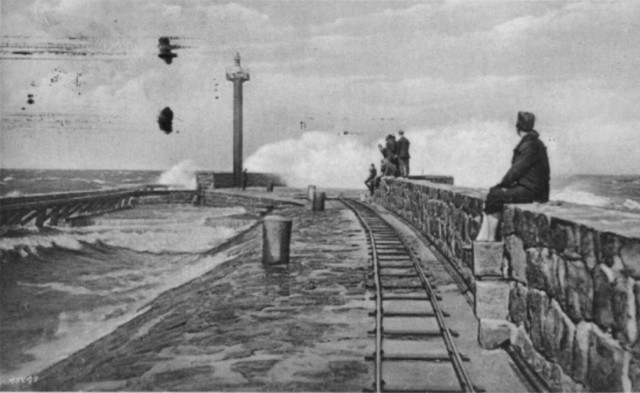 § Foto1 – Końcówka wschodniego pirsu kołobrzeskiego portu na pocztówce nadanej w 1927 r. Zwracają uwagę wąskie tory biegnące niemal do główki.