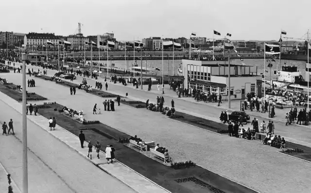 " Gdynia – Aleja Zjednoczenia (ob. Al. Jana Pawła II)

Opis Obiektu:
Fotografia czarno-biała przedstawia Aleję Zjednoczenia na molo Południowym. Nazwana tak została na cześć zjednoczenia ziem polskich po I wojnie światowej (obecnie al. Jana Pawła II). Z prawej strony, na nabrzeżu Pomorskim, budowana w latach 1937-38 przystań pasażerska Żeglugi Polskiej. W głębi gmachy przy ul. Waszyngtona, m.in. biurowiec Żeglugi Polskiej (obecnie siedziba Dowództwa Floty) oraz Instytut Meteorologii i Gospodarki Wodnej z ażurową wieżą. Na zdjęciu ujęci zostali spacerowicze. Na masztach, wzdłuż Alei, powiewają flagi Żeglugi Polskiej i narodowe. "