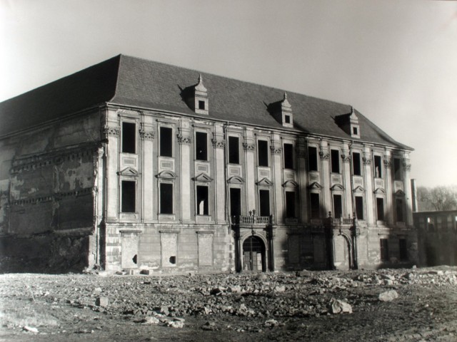 Fotografia wykonana przez Józefa Drzazgę w 1961 r. – kamienicy już nie ma, pałac stoi osamotniony, na jego fasadzie kładą się cienie wież kościoła pw. Wniebowzięcia NMP. Wokół pustka. Pałac czeka na czas swojej odbudowy.