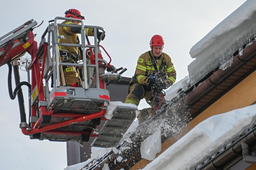 Strażacy musieli skuwać lód i śnieg na dachu budynku, w...