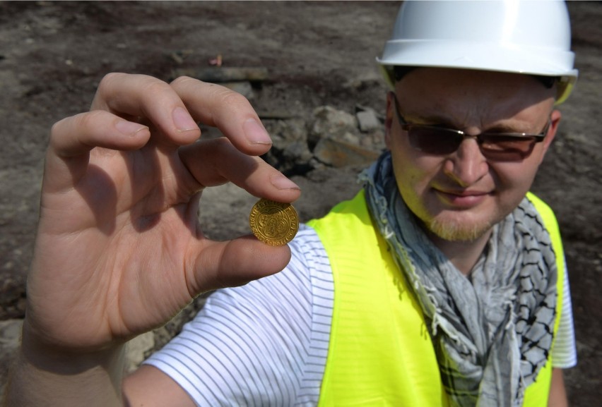 Archeolog Jakub Prager demonstruje znalezioną złotą monetę....