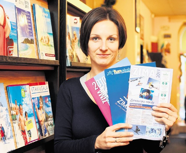 Emilia Brożyna z biura podróży przy al. Kościuszki pokazuje katalogi ofert zimowych.