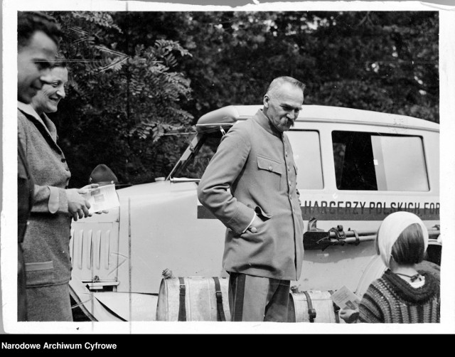 Marszałek Józef Piłsudski w czasie rozmowy z córką Jadwigą (z prawej). Widoczni także: harcerz Jerzy Jeliński (1. z lewej) i żona marszałka Aleksandra Piłsudska (2. z lewej). W głębi widoczny samochód Ford T.