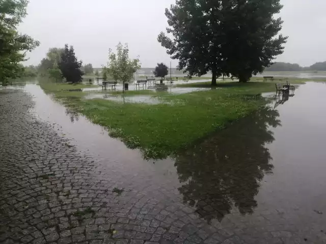 Wody Wisły powoli wdzierają się na Bulwar Piłsudskiego od strony rzecznego portu, gdzie  cumują statki.