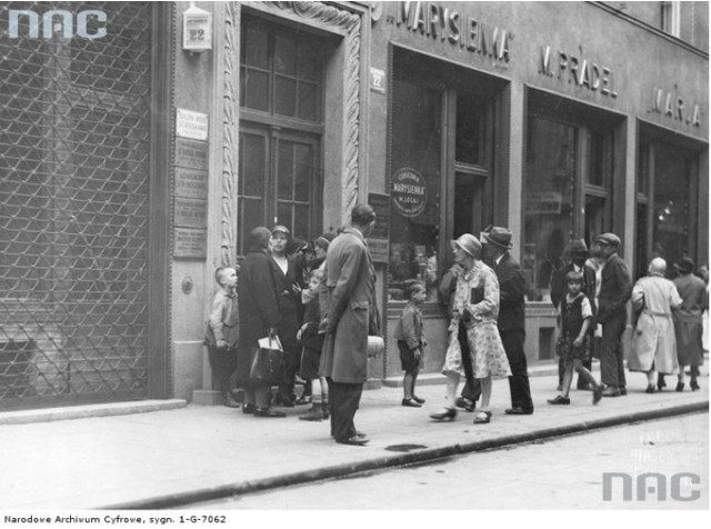 Ludzie stojący przed wejściem do cukierni "Marysieńka". Widoczne na budynku szyldy reklamowe (brak daty).