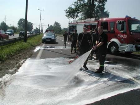 Strażacy zmywają ślady po przewróconej przyczepie.