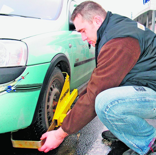 Szymon Sowula z Autoclambu blokuje koło auta stojącego w niedozwolonym miejscu.