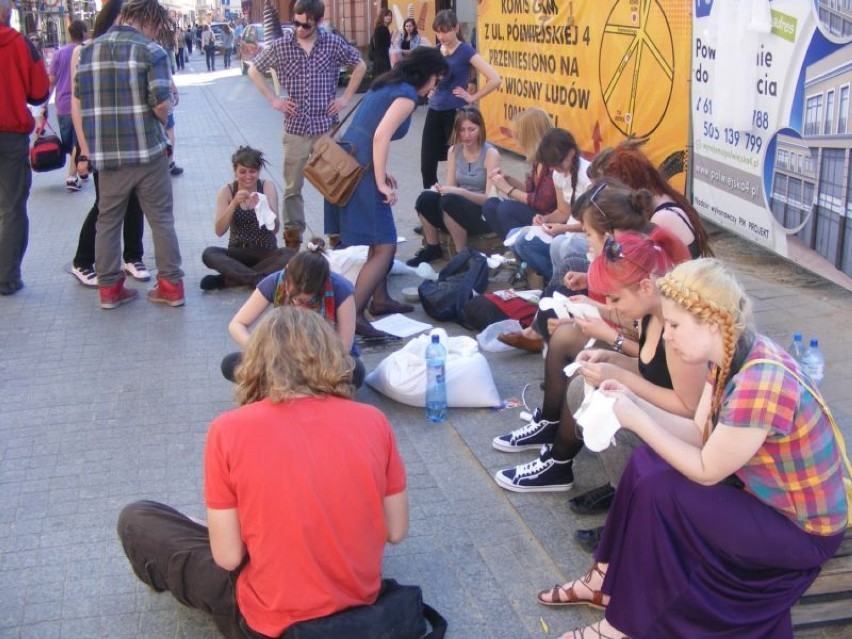Grupa młodych ludzi siedząc na chodniku, szyła małe laleczki...