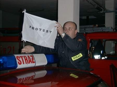 Młodszy ogniomistrz Marek Plichta, członek komitetu protestacyjnego zmiany nr 1, wiesza flagę na strażackim wozie.