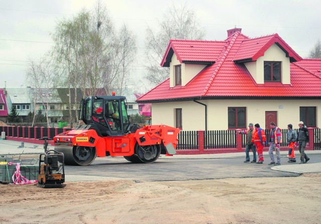 Drogowcy układają asfalt na ulicy, przy której dopiero budowane są domki jednorodzinne
