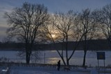 Śnieg i mróz królują na dworze. Jezioro Miejskie w okowach zimy o zachodzie słońca, w barwach błękitu i lekkiej żółci, wygląda pięknie
