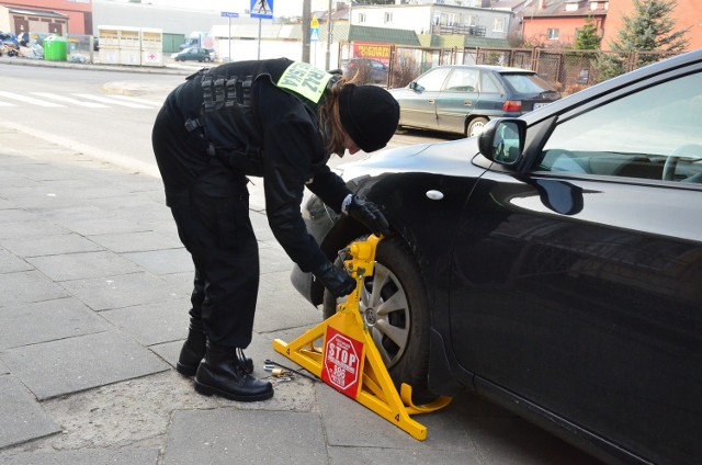 Blokadę na koło źle zaparkowanego samochodu zakłada Agata Kapuścińska, młodszy strażnik