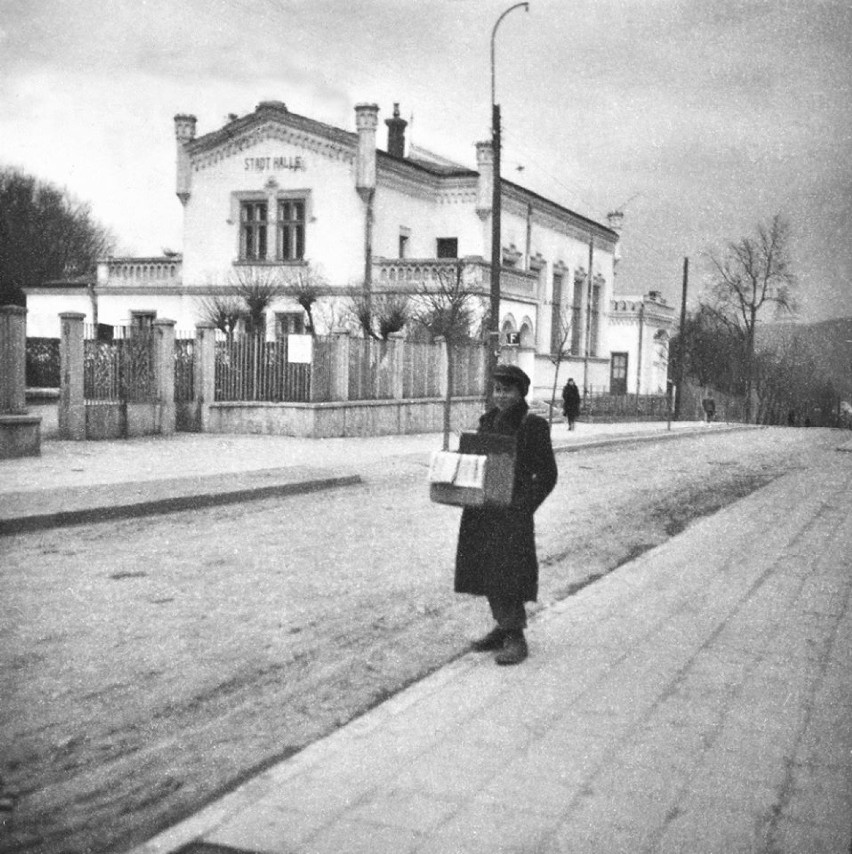 Zdzisław Beksiński jako kolporter na tle budynku Sokoła w Sanoku zamienianego przez Niemców na Stadt Halle, lata 40. XX w.