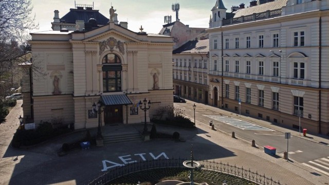 Zdjęcie budynku teatru. Tuż przed wejściem namalowany białą farbą wielki napis cyrylicą: DETI. 

Zobacz kolejne zdjęcia. Przesuwaj zdjęcia w prawo - naciśnij strzałkę lub przycisk NASTĘPNE