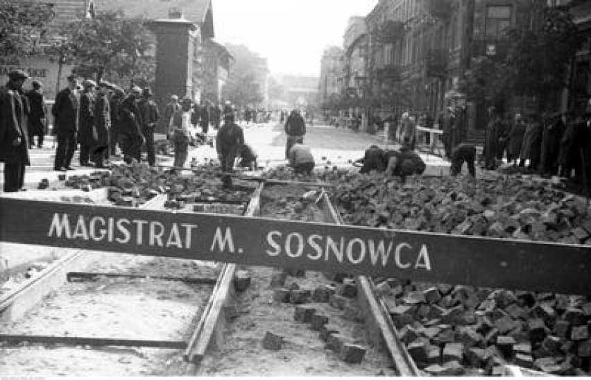 Układanie bruku na jezdni i torowisku. Widoczni przechodnie,...