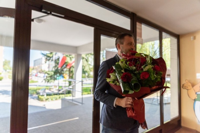 Zastępca burmistrza w maseczce i rękawiczkach z kwiatami w bibliotece