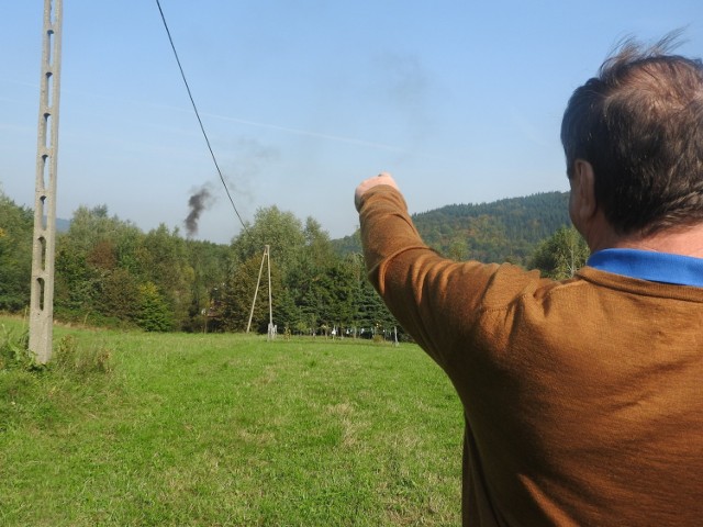 Zaraz za drzewami jest zakład meblarski, który, zdaniem protestujących mieszkańców wsi, zatruwa ich wydobywającym się z wysokiego komina, czarnym i gęstym dymem