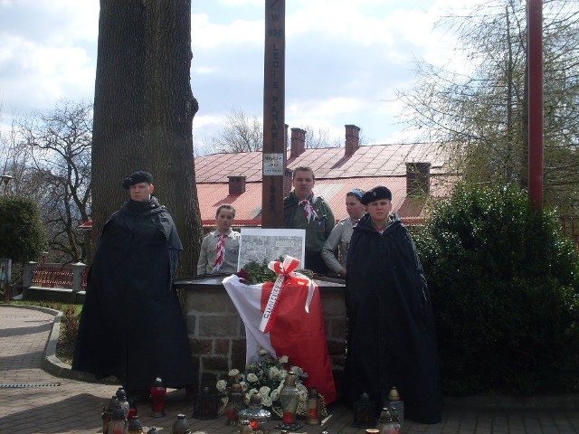 Pod drewnianym krzyżem przy kościele w Radziechowach znajduje się tablica ze zdjęciami wszystkich osób, które zginęły pod Smoleńskiem. Ludzie modlą się w tym miejscu i zapalają znicze.