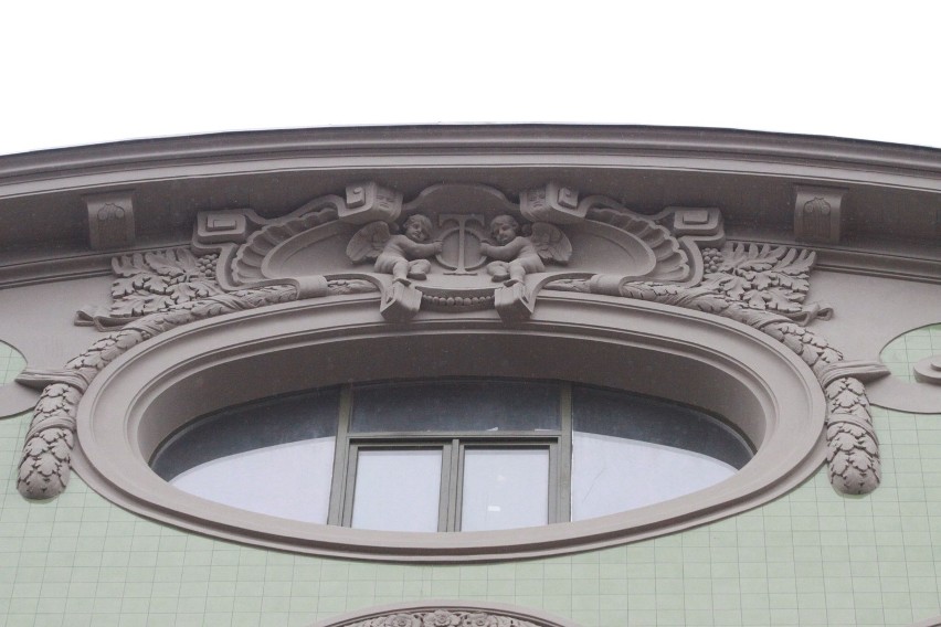Nad oknem ozdobionym liśćmi dwa anioły z monogramem "TO"