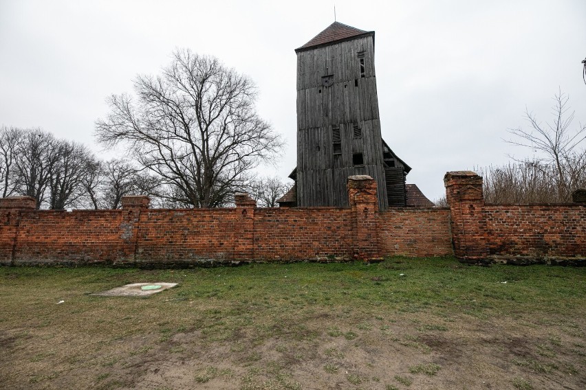 Dzwonnica wystaje ponad ogrodzenie z cegieł.